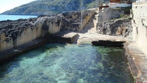 Una piscina cristalina con escalones que bajan al agua, rodeada de muros de piedra y vista al mar.