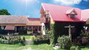 A traditional wooden house with a red roof, a front porch, and a garden with a wooden fence and steps leading to the entrance. - Conacul Bunicilor (Baia de Fier)