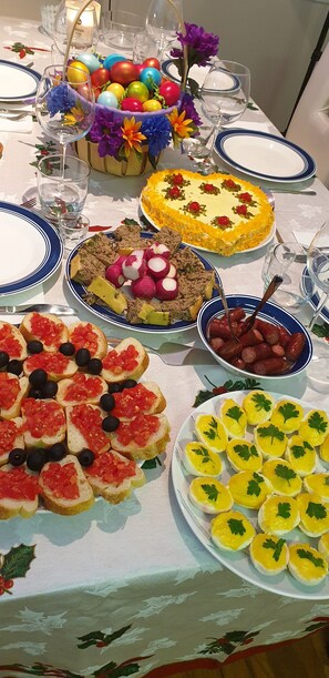 A table set with various dishes, including a cake, appetizers, and a centerpiece with colorful eggs and flowers. - Conacul Bunicilor (Baia de Fier)