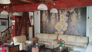 A living room with a beige sofa, two coffee tables, and a large floral mural on the wall. - Conacul Bunicilor (Baia de Fier)