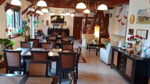 A cozy dining area with wooden tables and chairs, surrounded by potted plants and a television. - Conacul Bunicilor (Baia de Fier)
