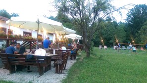 An outdoor dining area with wooden tables and benches, umbrellas, and a volleyball net. - Conacul Bunicilor (Baia de Fier)