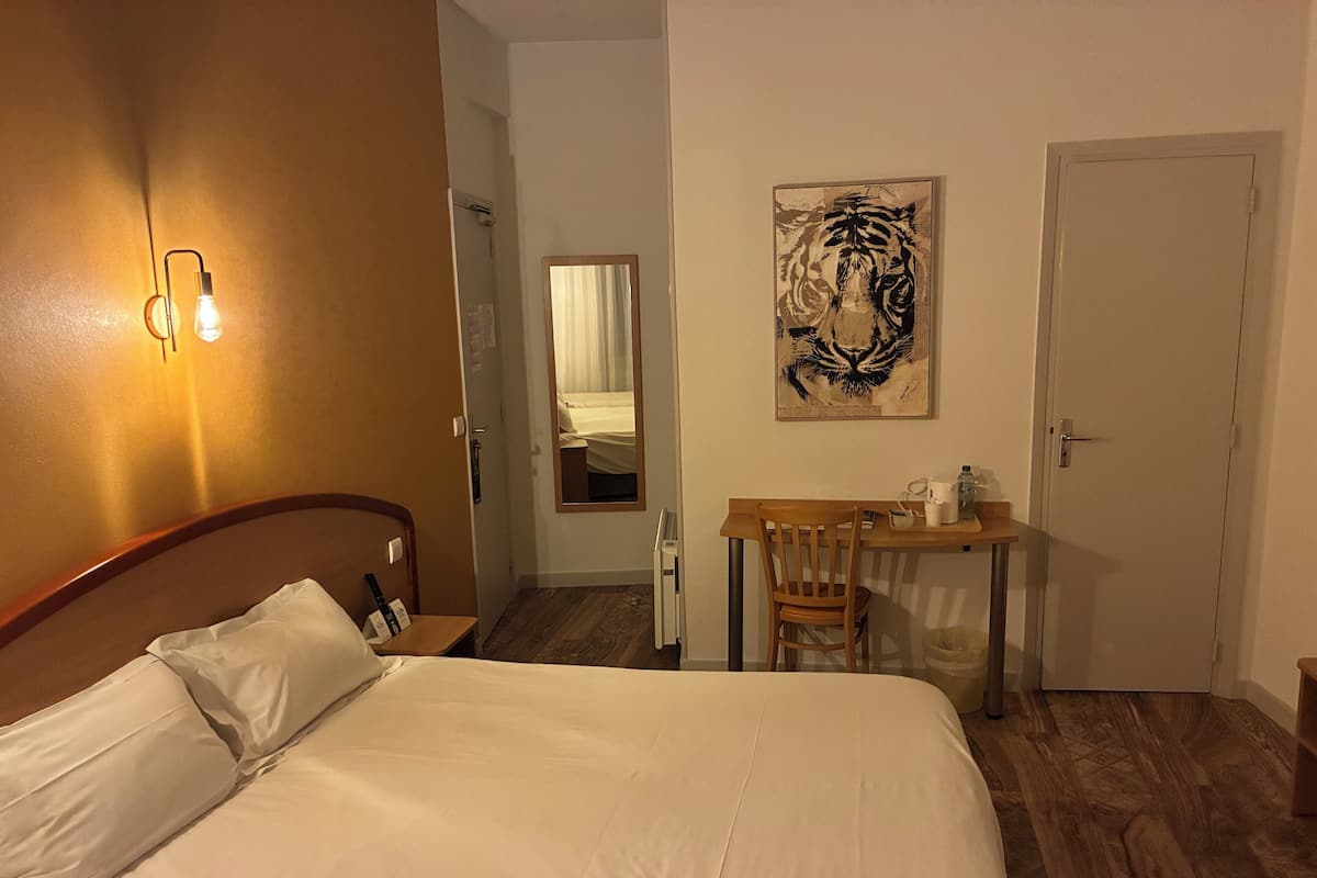 A hotel room with a bed, a desk, a chair, a mirror, and a door.