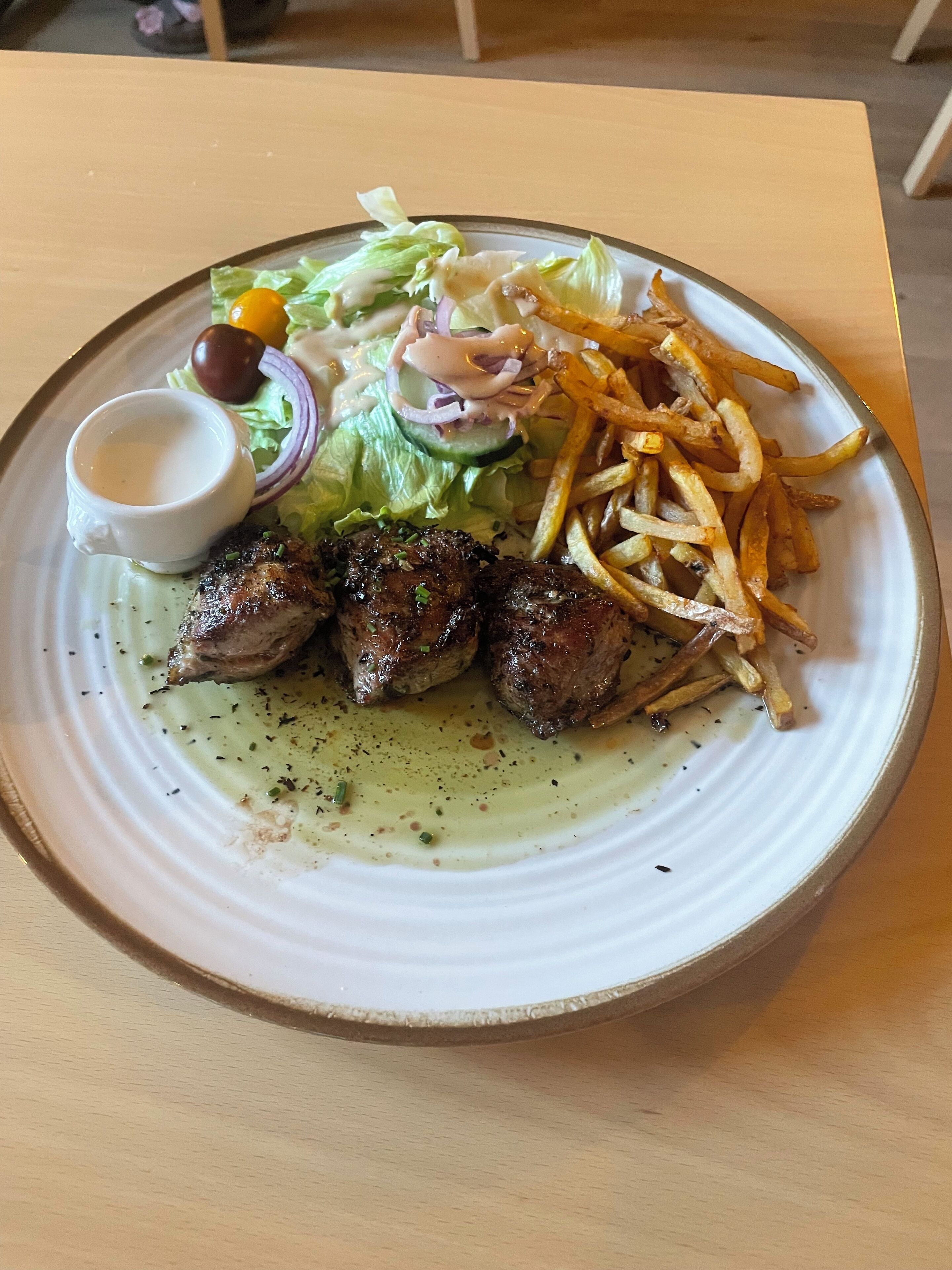 Un plato con carne a la parrilla, papas fritas, ensalada y un recipiente pequeño con salsa.