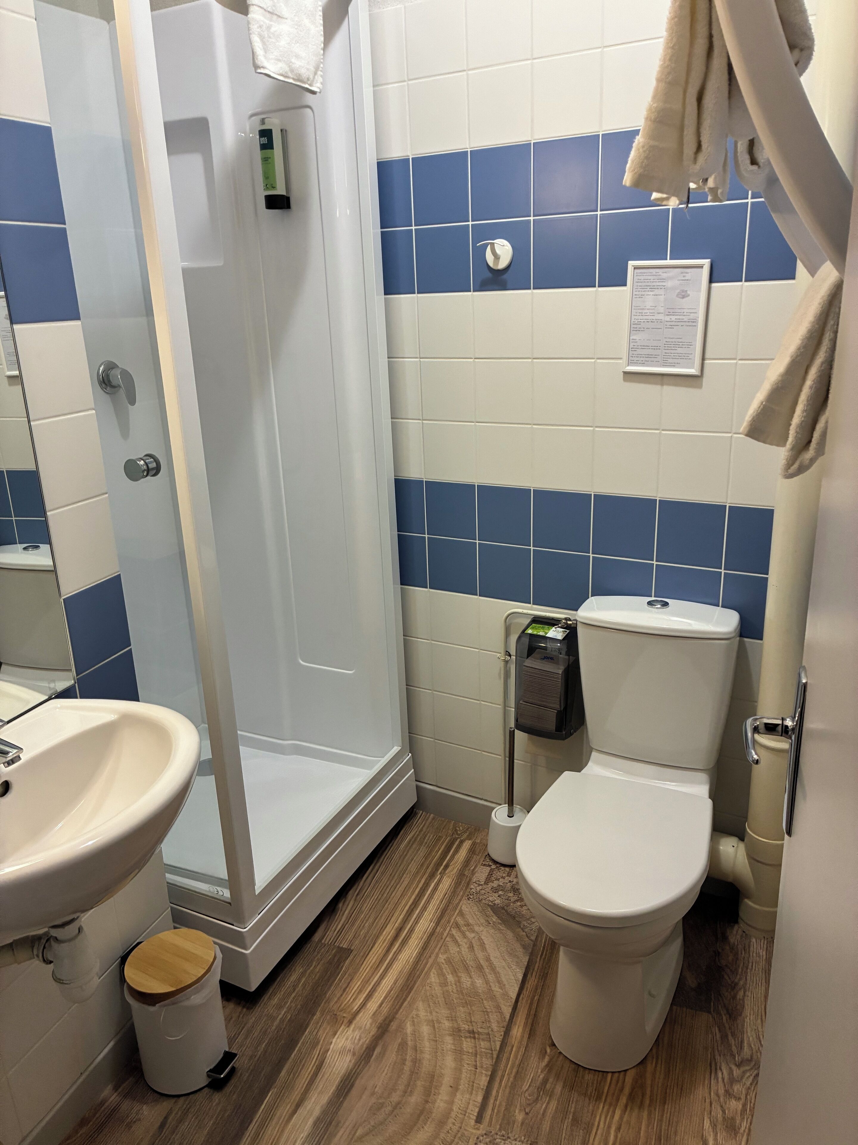 A bathroom with a shower, toilet, sink, and a trash bin.