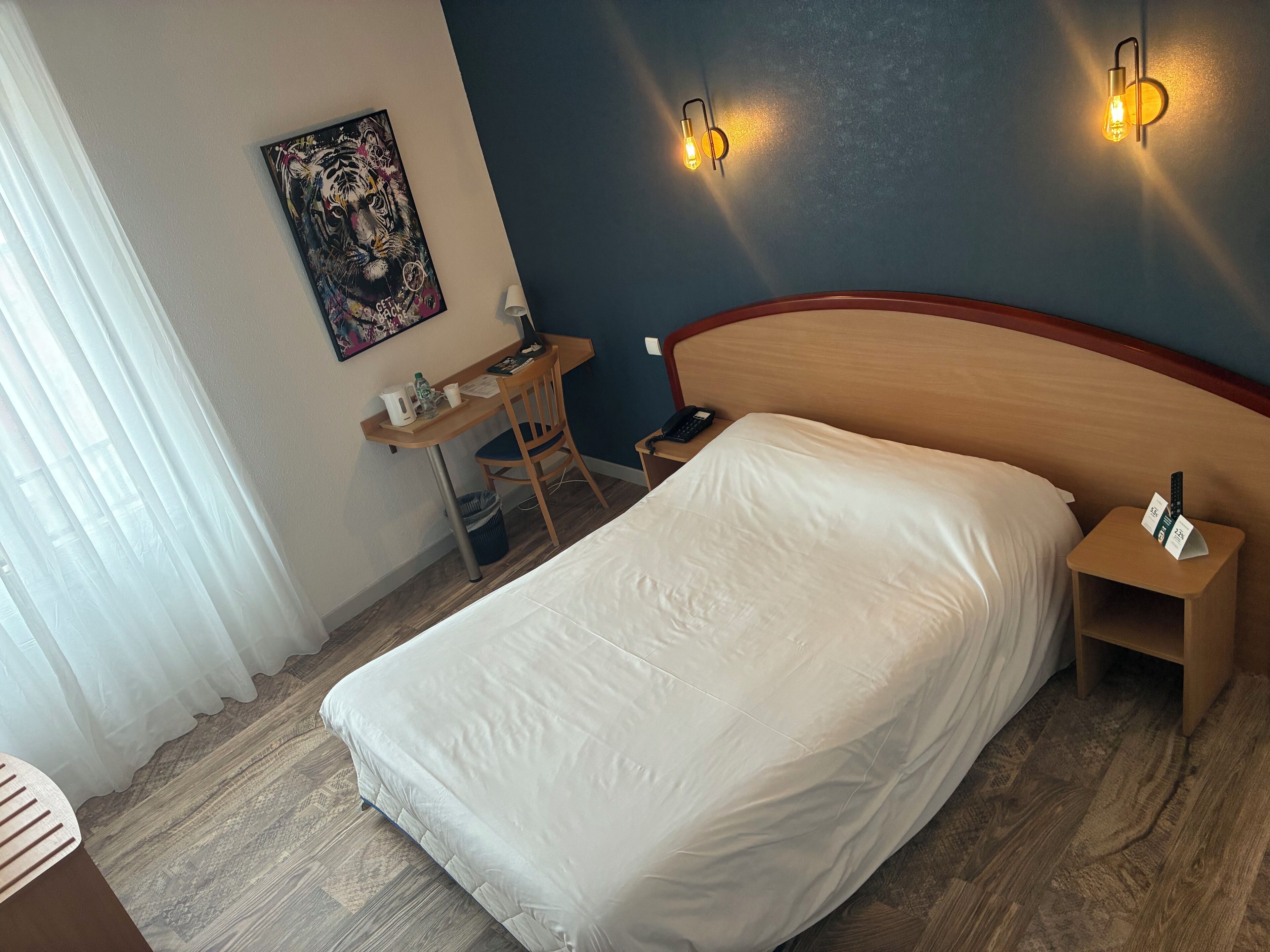 A hotel room with a bed, a desk, a chair, a telephone, and a wall-mounted light fixture.