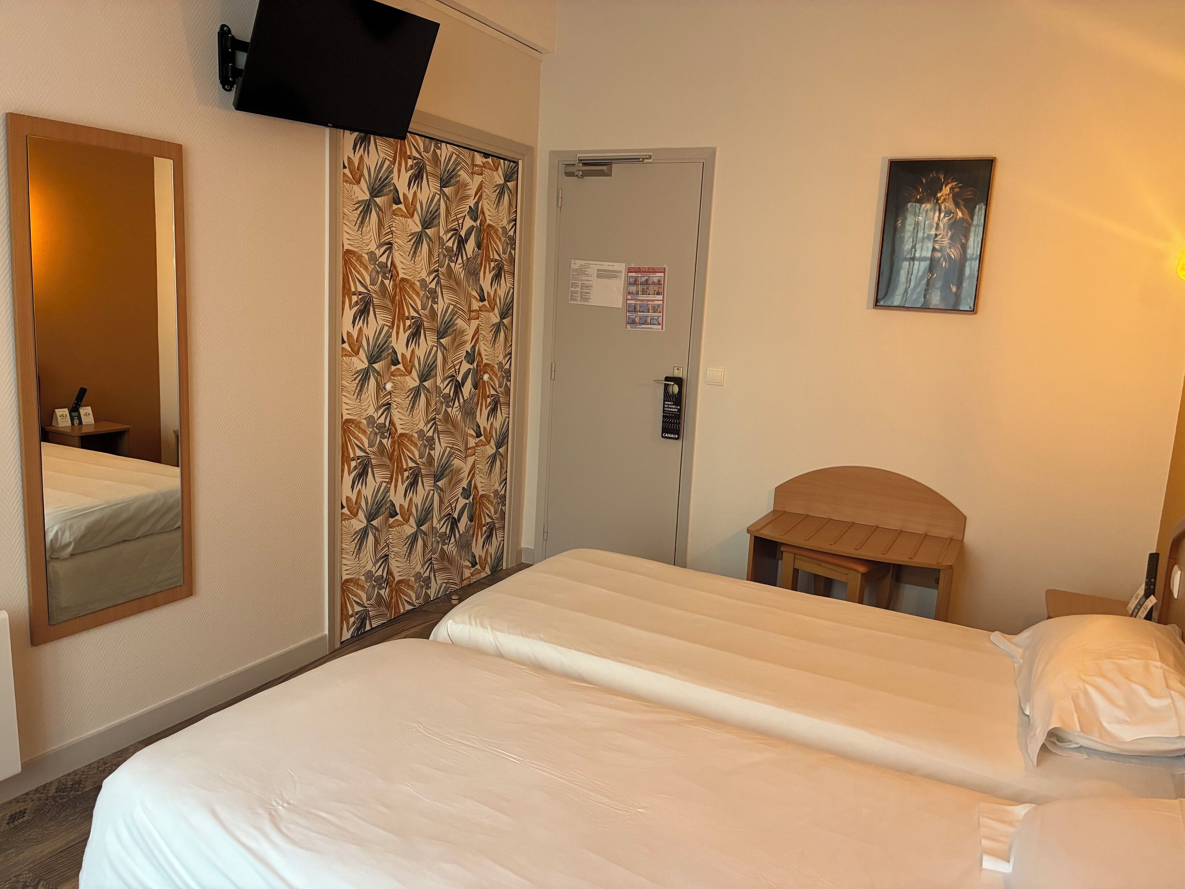 Et hotelværelse med seng, spejl, garderobeskab, dør og et lille bord.