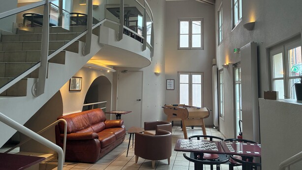 A spacious interior with a curved staircase, a leather sofa, a foosball table, and a dining area with a chessboard. - Hotel du Commerce (Volvic)