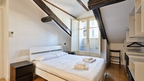 A bedroom with a bed, a nightstand, a window, and a wooden ceiling beam. - GuestHost - Cozy and modern flat 80sqm with all the comfort, convenient for its position in the city center of Turin, very close to the main points of interest of the city as the Egyptian Museum, only 500m away, Piazza Solferino (400m), and Giardini Real (Torino)