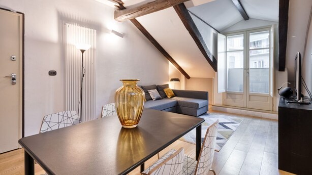 A modern living room with a dining table, sofa, and a large window. - GuestHost - Cozy and modern flat 80sqm with all the comfort, convenient for its position in the city center of Turin, very close to the main points of interest of the city as the Egyptian Museum, only 500m away, Piazza Solferino (400m), and Giardini Real (Torino)