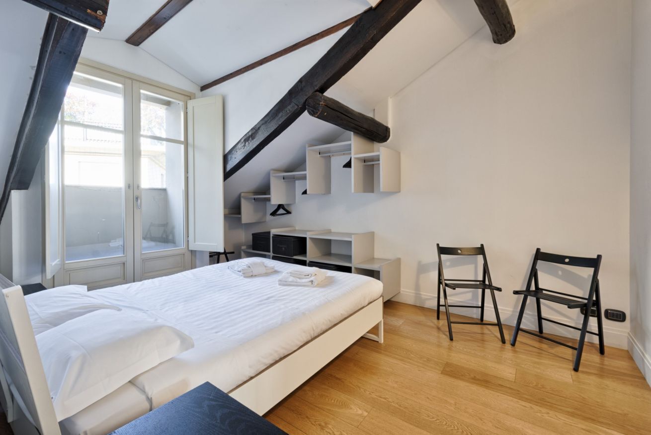 A bedroom with a bed, a window, a desk, and two chairs.