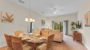 Un coin repas avec des chaises en osier et une table dressée pour six personnes, un ventilateur de plafond et des œuvres d’art accrochées aux murs.
