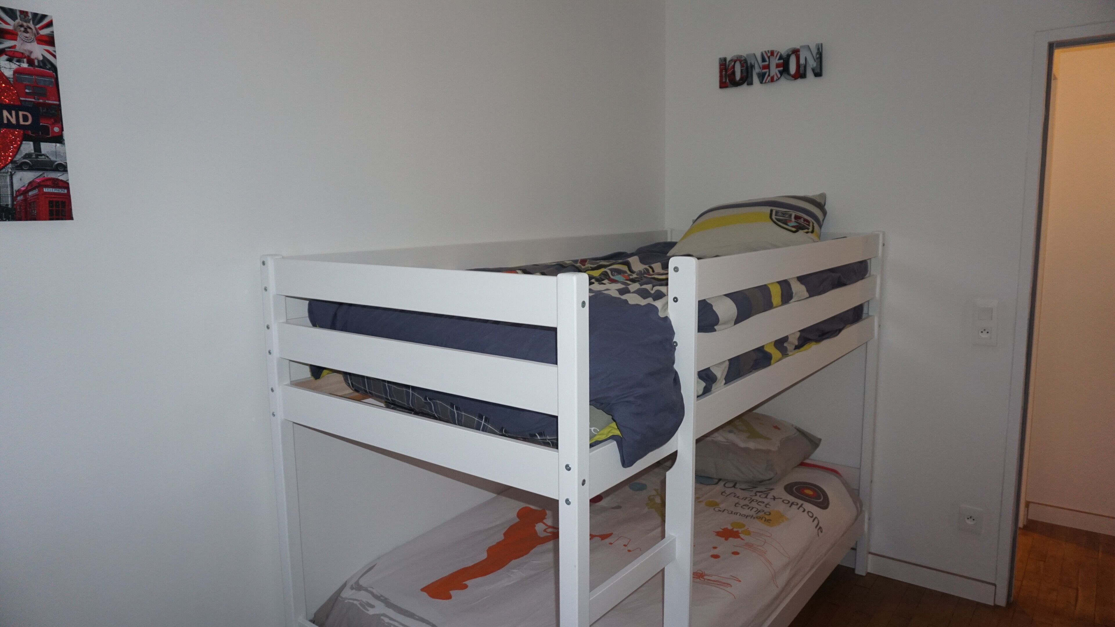 A bunk bed in a room with a poster on the wall and a door to the right.
