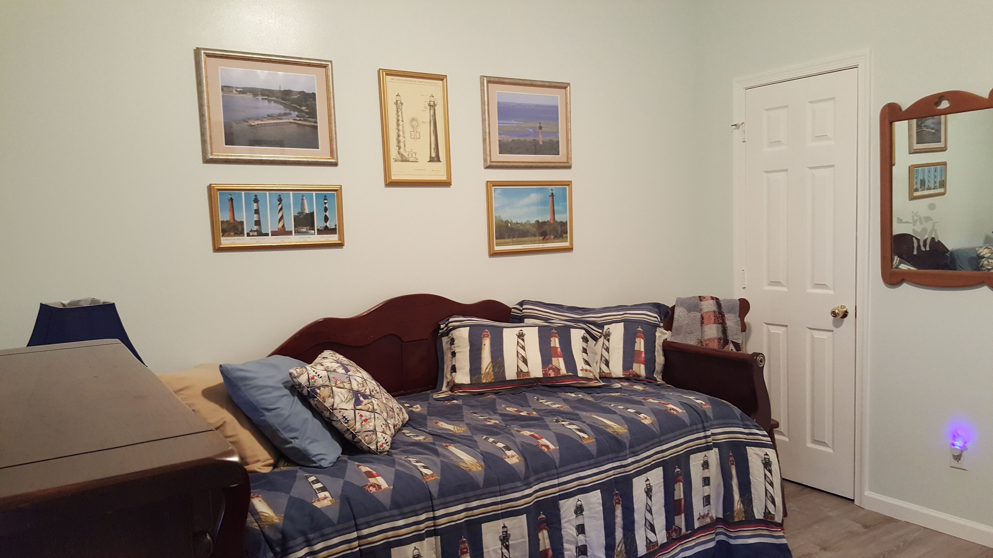 A bedroom with a bed, a dresser, a door, and four framed pictures on the wall.