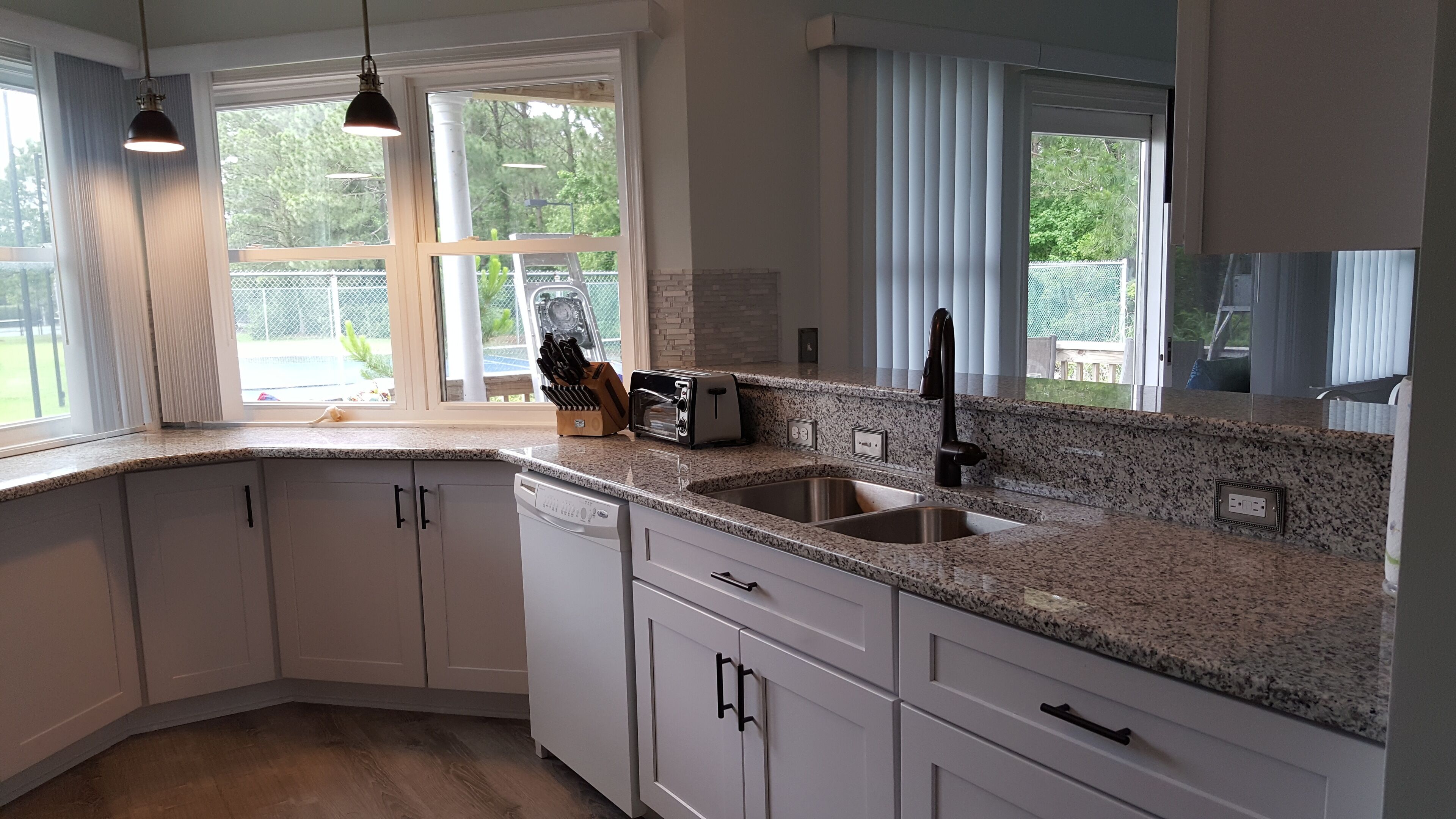 A modern kitchen with white cabinets, granite countertops, a built-in dishwasher, and a stainless steel sink.