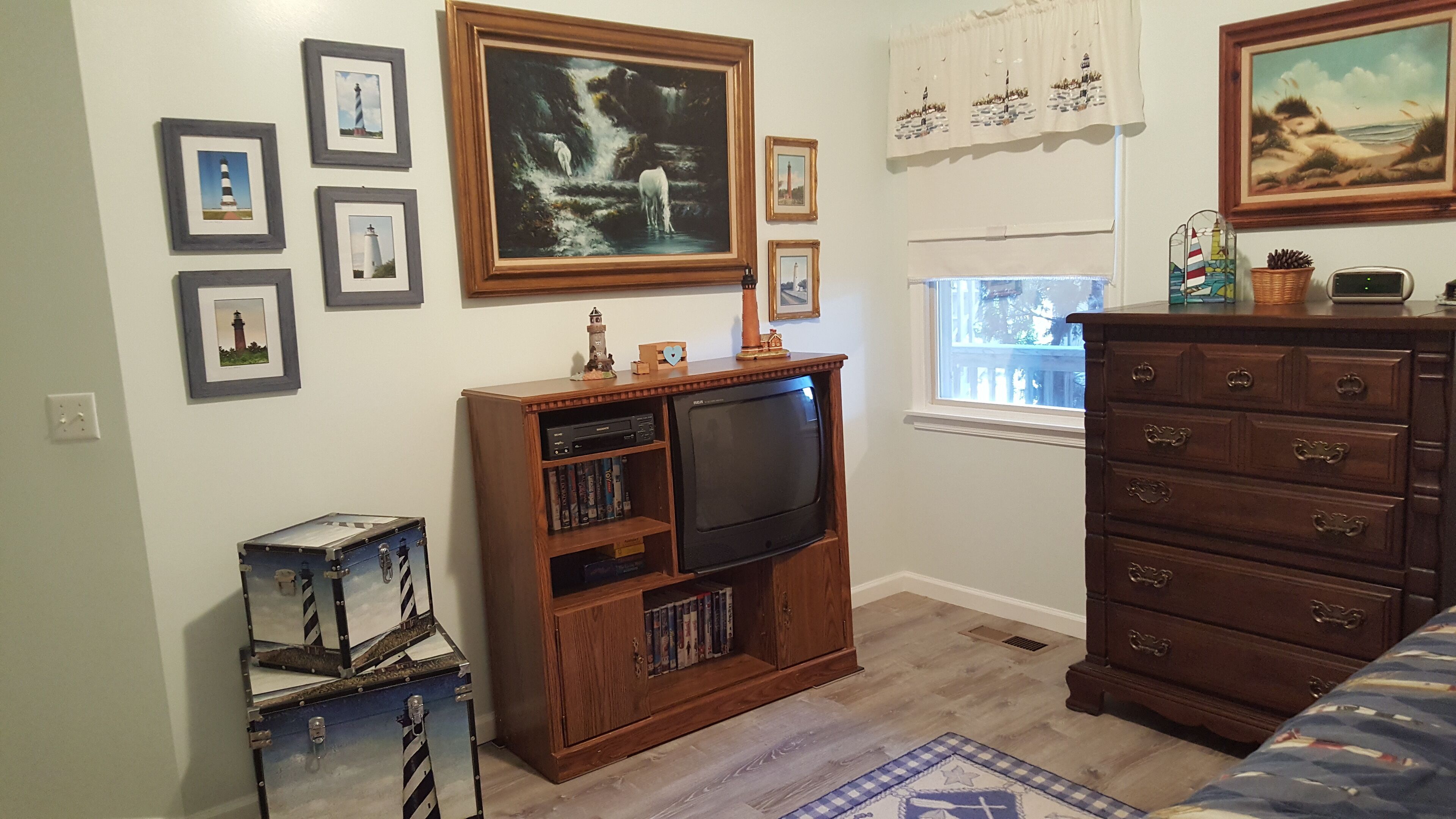 Een kamer met een houten entertainmentkast, een televisie, een dressoir en verschillende ingelijste foto’s aan de muur.
