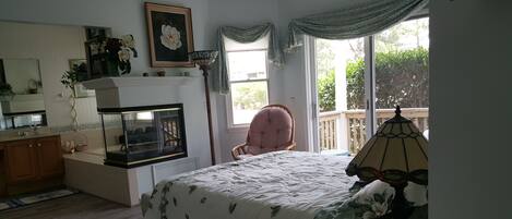 A bedroom with a bed, a chair, a nightstand, a lamp, a window, and a fireplace.