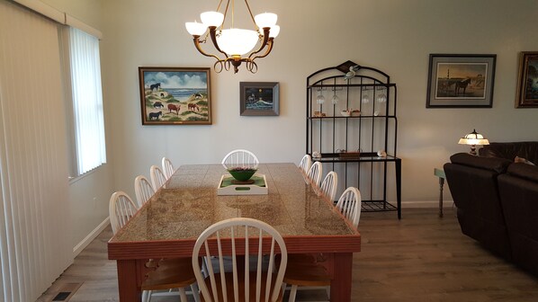 A dining area with a long table, white chairs, a chandelier, and artwork on the walls. - Comfort Zone in Corolla Light Resort ADA‑Friendly, Dog‑Friendly, Sat to Sat only (Corolla)