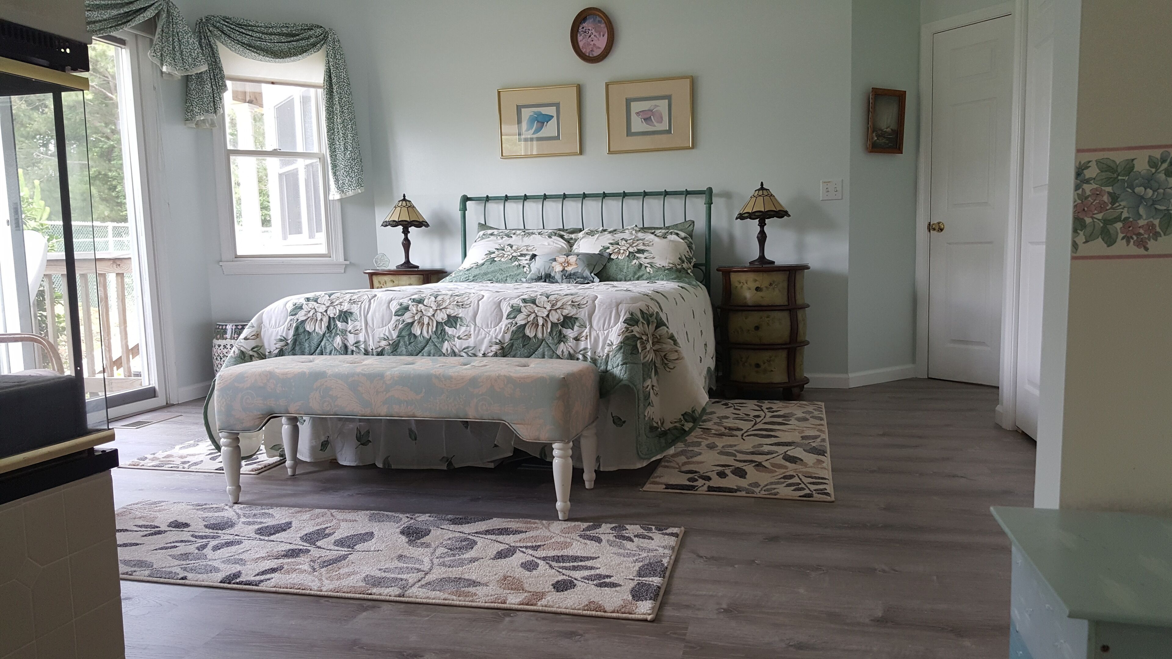 A bedroom with a bed, two bedside tables, a bench, a window with a view, and a door.