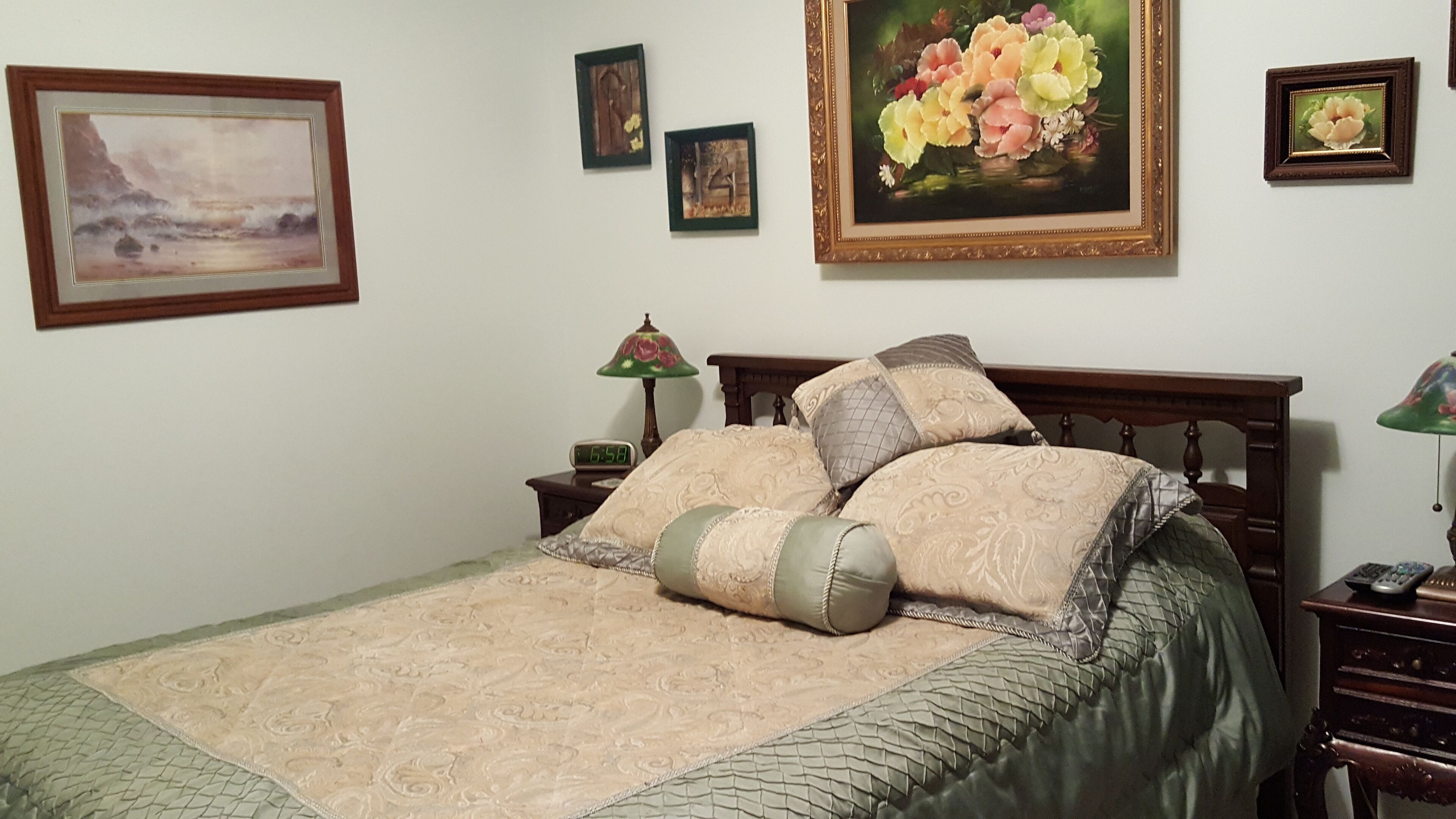 Quarto com cama, mesa de cabeceira, abajur e quadros na parede.