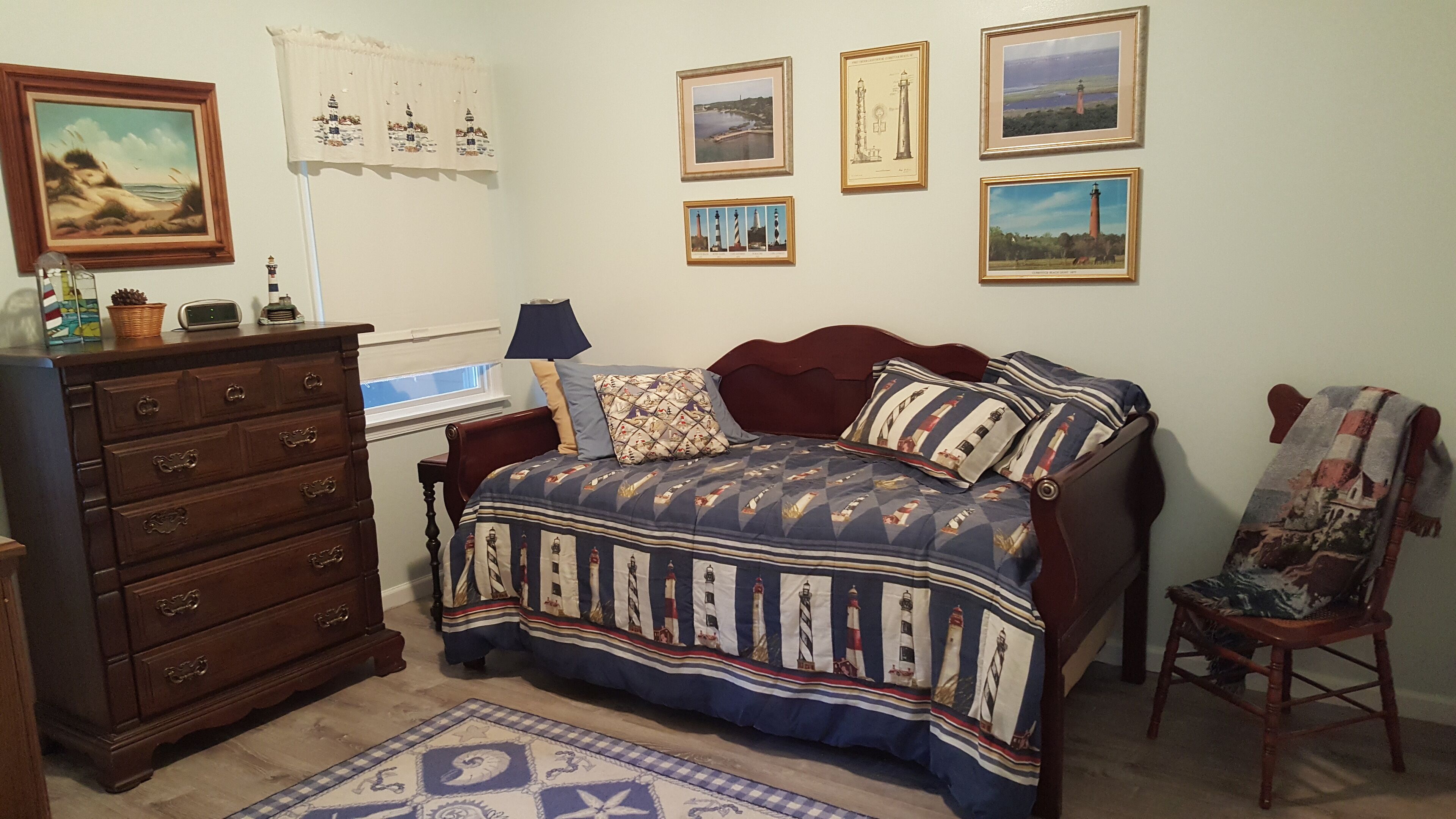 Een slaapkamer met een houten dressoir, een bed met een beddegoed met een patroon en een stoel met een plaid met een nautisch thema.