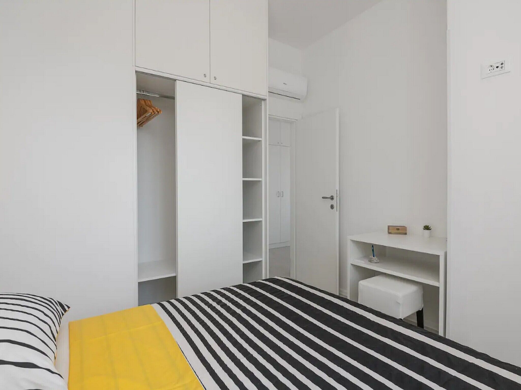 Una camera da letto con un letto, un armadio e una piccola mensola bianca.