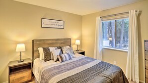 A neatly arranged bedroom with a bed, two bedside tables with lamps, a window with curtains, and a wall-mounted light fixture. - Base Camp Lassen Home 13 Mi to Volcanic Nat'l Park (Shingletown)