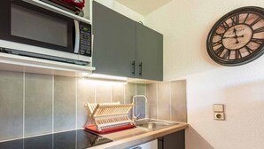 A compact kitchen with a microwave, a sink, and a clock on the wall.