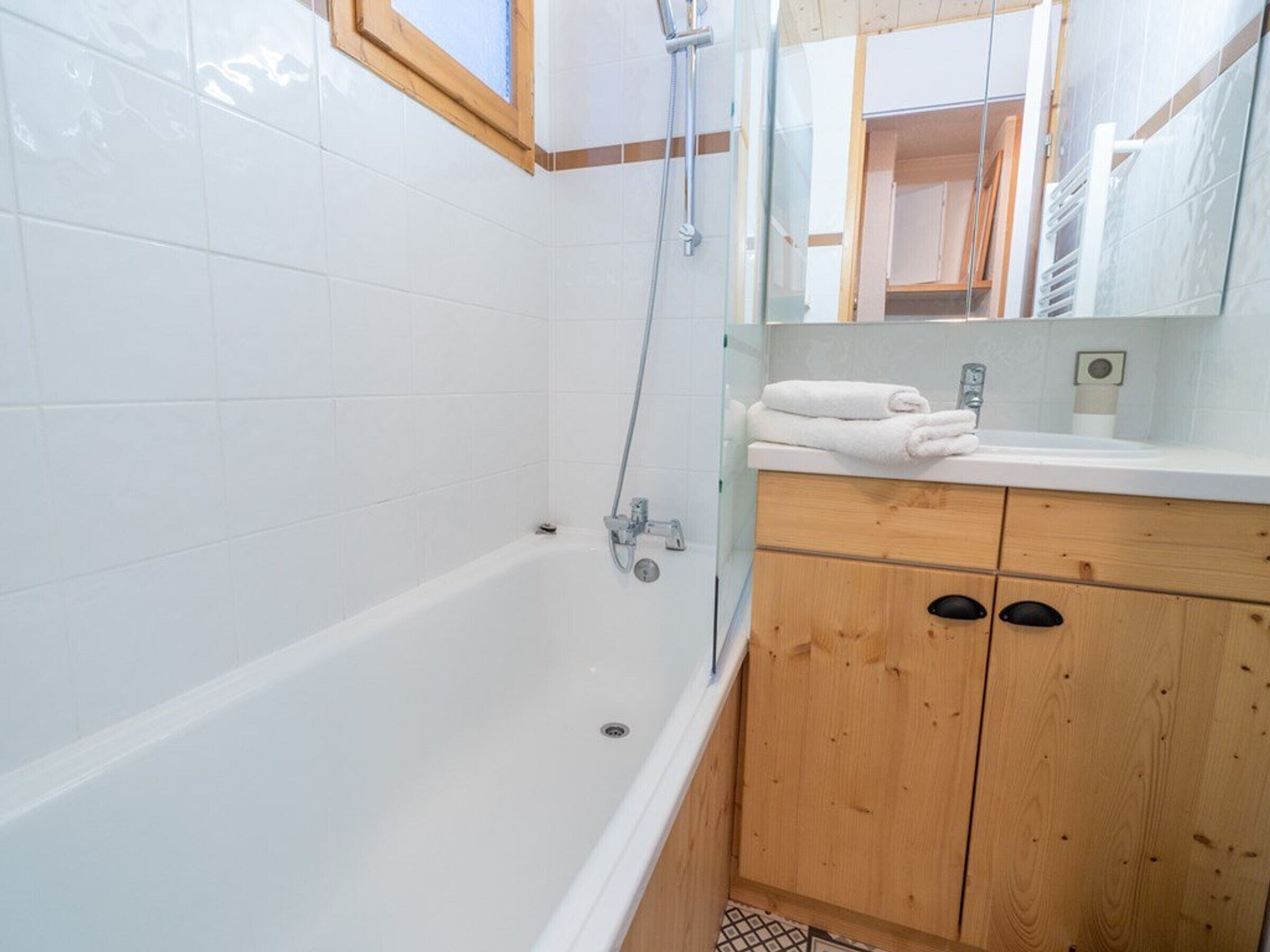 A bathroom with a bathtub, wooden cabinets, a mirror, and a window.