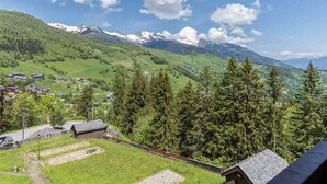 A mountainous landscape with a village, houses, and snow-capped peaks in the background.