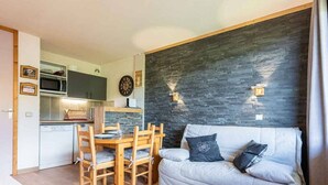 A compact living space with a kitchenette, a dining area with wooden furniture, and a sofa with cushions.