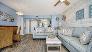 Un salon avec un canapé bleu clair, un fauteuil en osier, une table basse en bois et un ventilateur de plafond.