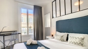 Une chambre d’hôtel avec un grand lit, un bureau, une chaise et une fenêtre donnant sur des immeubles.