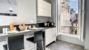 Une cuisine moderne avec un coin repas, une machine à café et une vue sur la ville, visible à travers une porte ouverte.