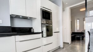 Une cuisine moderne avec des meubles blancs, un plan de travail noir, des appareils en acier inoxydable et un sol carrelé.