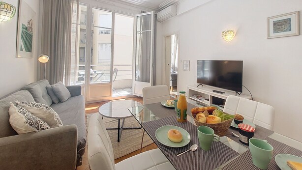 Una sala de estar moderna con un sofá, una mesa de centro, un televisor y un comedor con una mesa dispuesta para el desayuno.