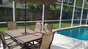 Un patio al aire libre con una mesa y sillas, una piscina y vistas a una valla de madera y árboles.