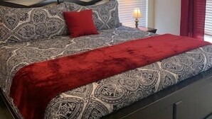 Un dormitorio con una colcha estampada, una manta roja y una mesita de noche con lámpara.