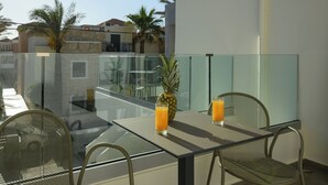 Ein Balkon mit einem Glastisch, zwei Stühlen, einer Ananas und zwei Gläsern Orangensaft.