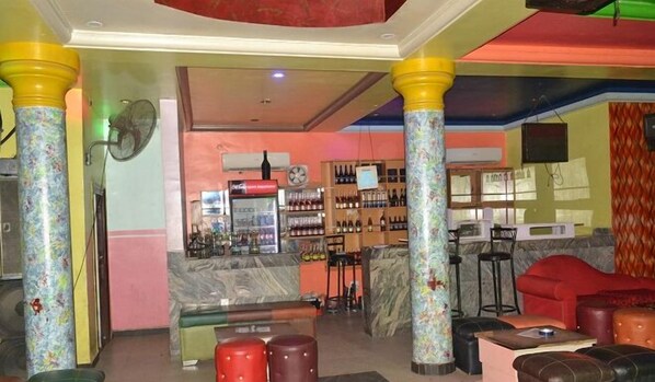 Zona de bar con mostrador, estanterías llenas de botellas y una zona de estar con taburetes.