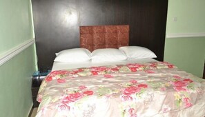 Een bed met een bloemenbedekking en witte kussens in een kamer met groene wanden en een donker houten hoofdbord.