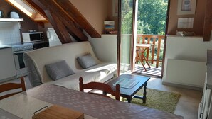 A cozy living room with a sofa, a dining table, and a kitchen area with a microwave and oven. - Mountain view. Sleeps 4. Calm. Private parking. Shaded. Close to hiking trails. (La Bresse)