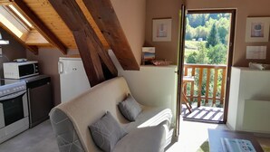 A cozy living room with a sofa, a coffee table, and a balcony with a wooden railing. - Mountain view. Sleeps 4. Calm. Private parking. Shaded. Close to hiking trails. (La Bresse)