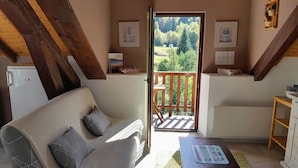 A cozy room with a sofa, a small table, and a view of a balcony with a wooden railing. - Mountain view. Sleeps 4. Calm. Private parking. Shaded. Close to hiking trails. (La Bresse)