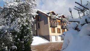 A two-story chalet with a wooden facade, balconies, and a snow-covered landscape. - Mountain view. Sleeps 4. Calm. Private parking. Shaded. Close to hiking trails. (La Bresse)