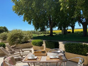 An outdoor seating area with tables and chairs, overlooking a landscaped garden and fields.