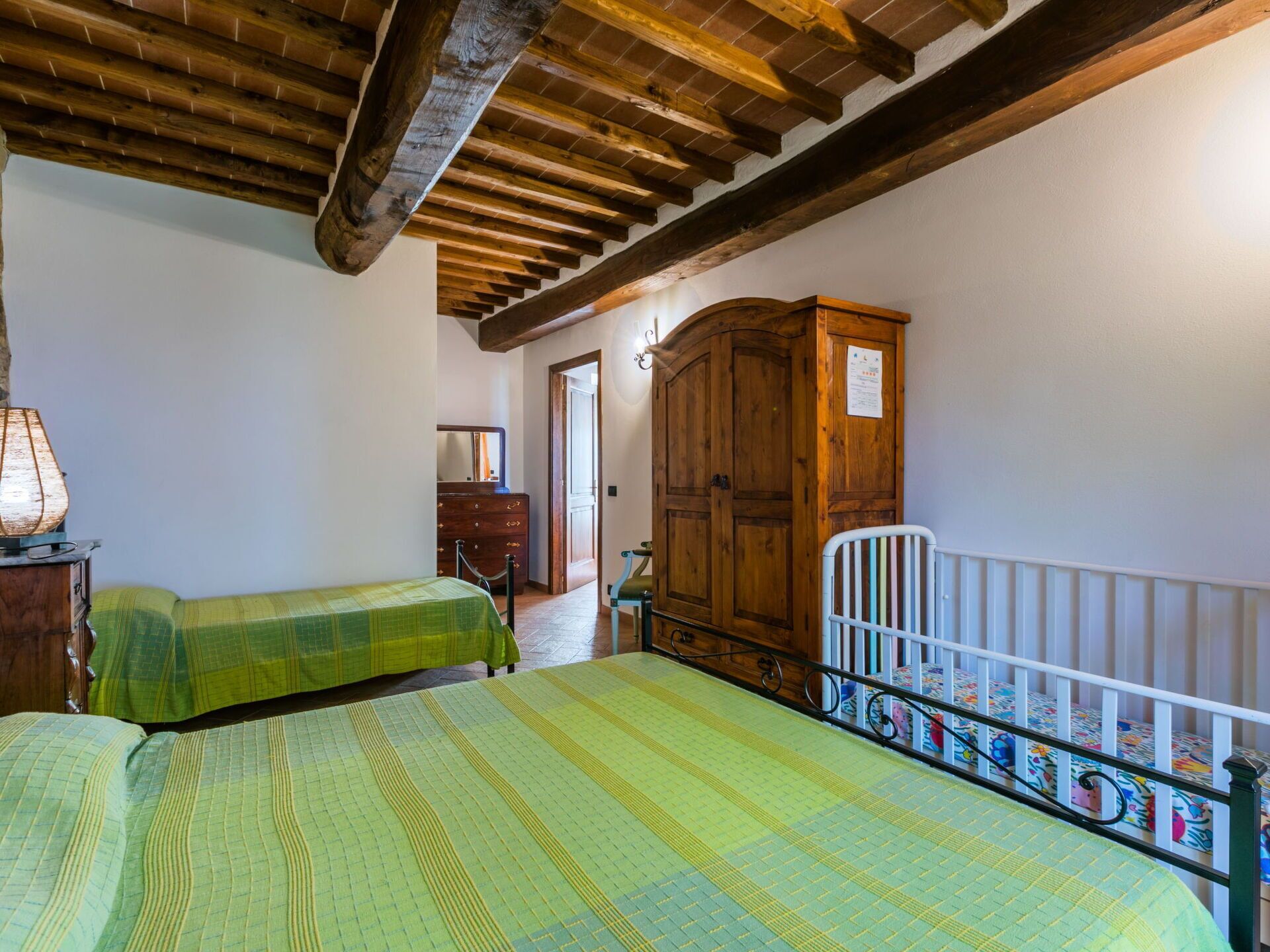 A bedroom with two beds, wooden beams on the ceiling, a wardrobe, and a crib.