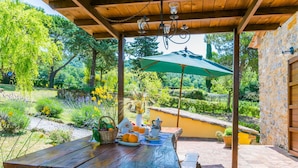 A wooden pergola with a table set for a meal, surrounded by a garden with various plants and flowers. - Cosy apartment for 12 people with private pool, A/C, WIFI, TV, patio and pets allowed (Castelnuovo Di Val Di Cecina)
