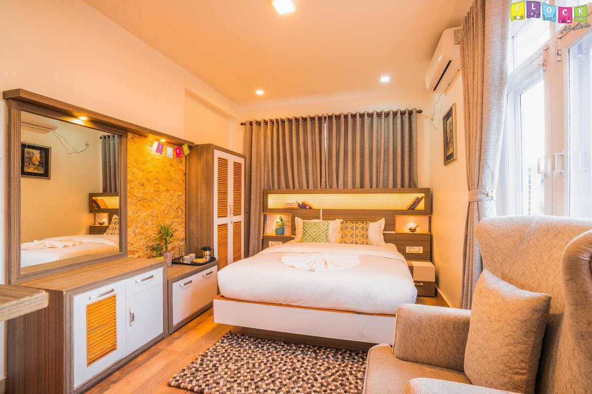 A hotel room with a large bed, a sitting area, a vanity with a mirror, and a window with curtains.