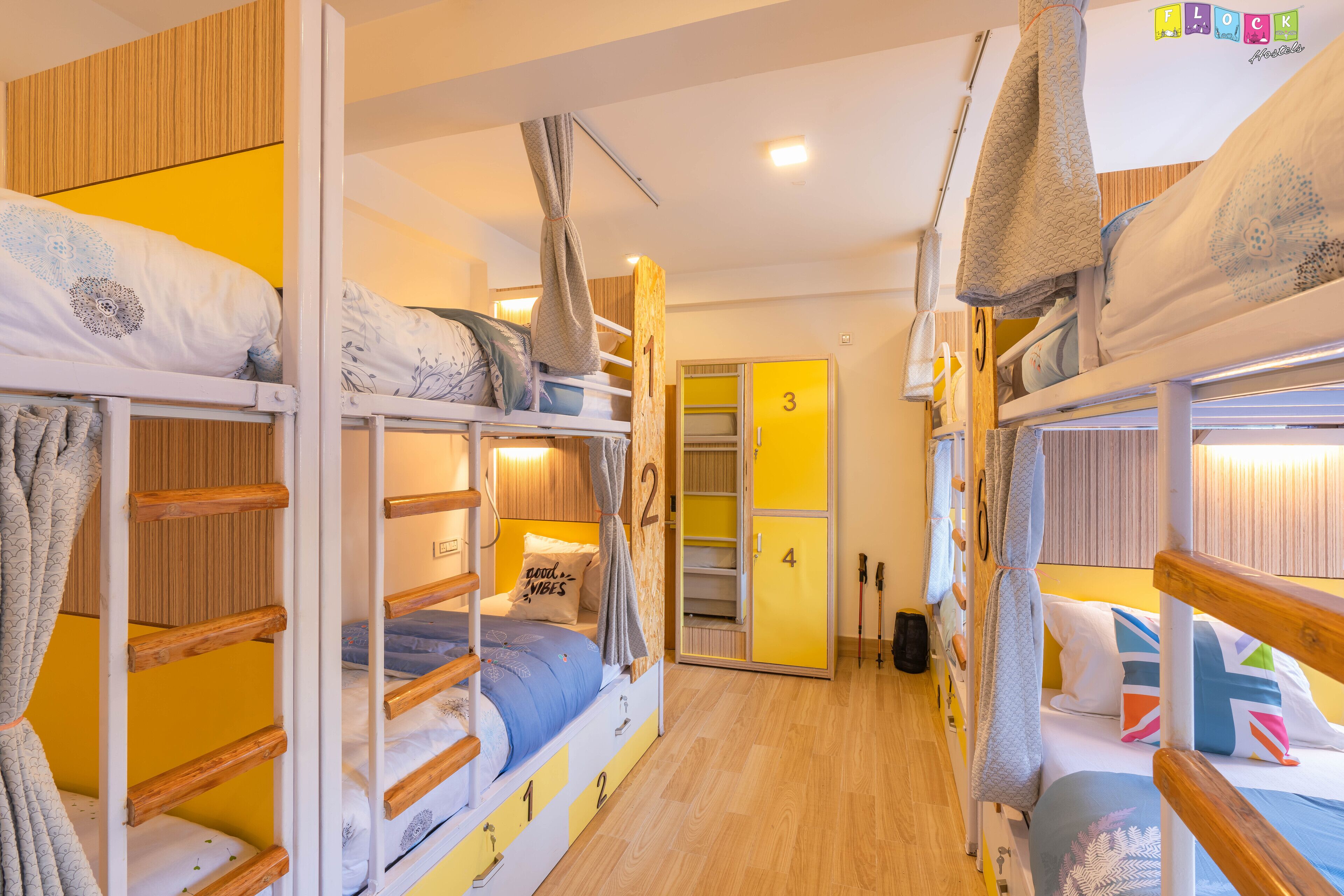 A dormitory room with bunk beds, wooden walls, and a yellow door.
